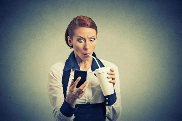 A young woman drinks soda and looks at her phone