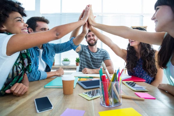 Excited young workers put their hands together over a work table symbolizing teamwork