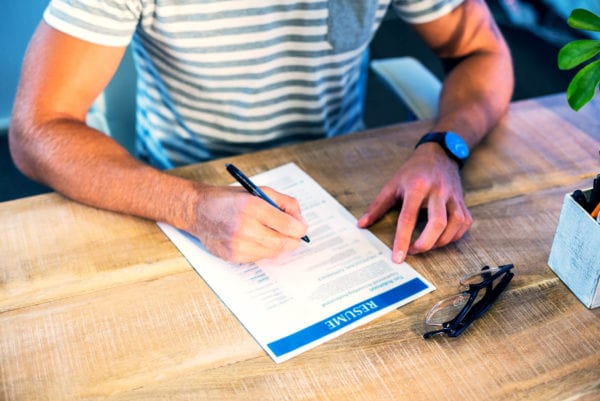 A man sits at a modern desk, pen in hand, editing his resume.