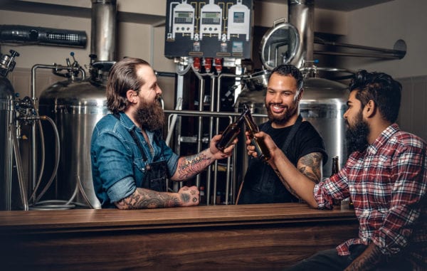 Three brewery workers enjoy a beer in front of the stills