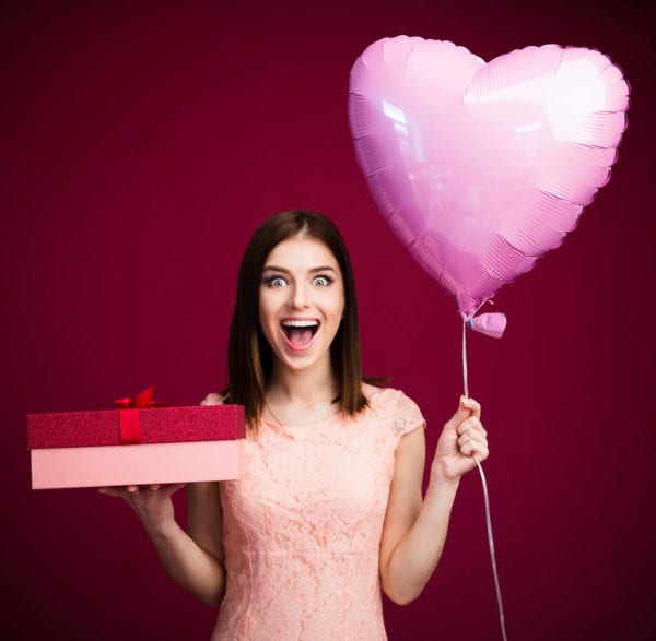 A young woman holds a heart shaped balloon and a gift box