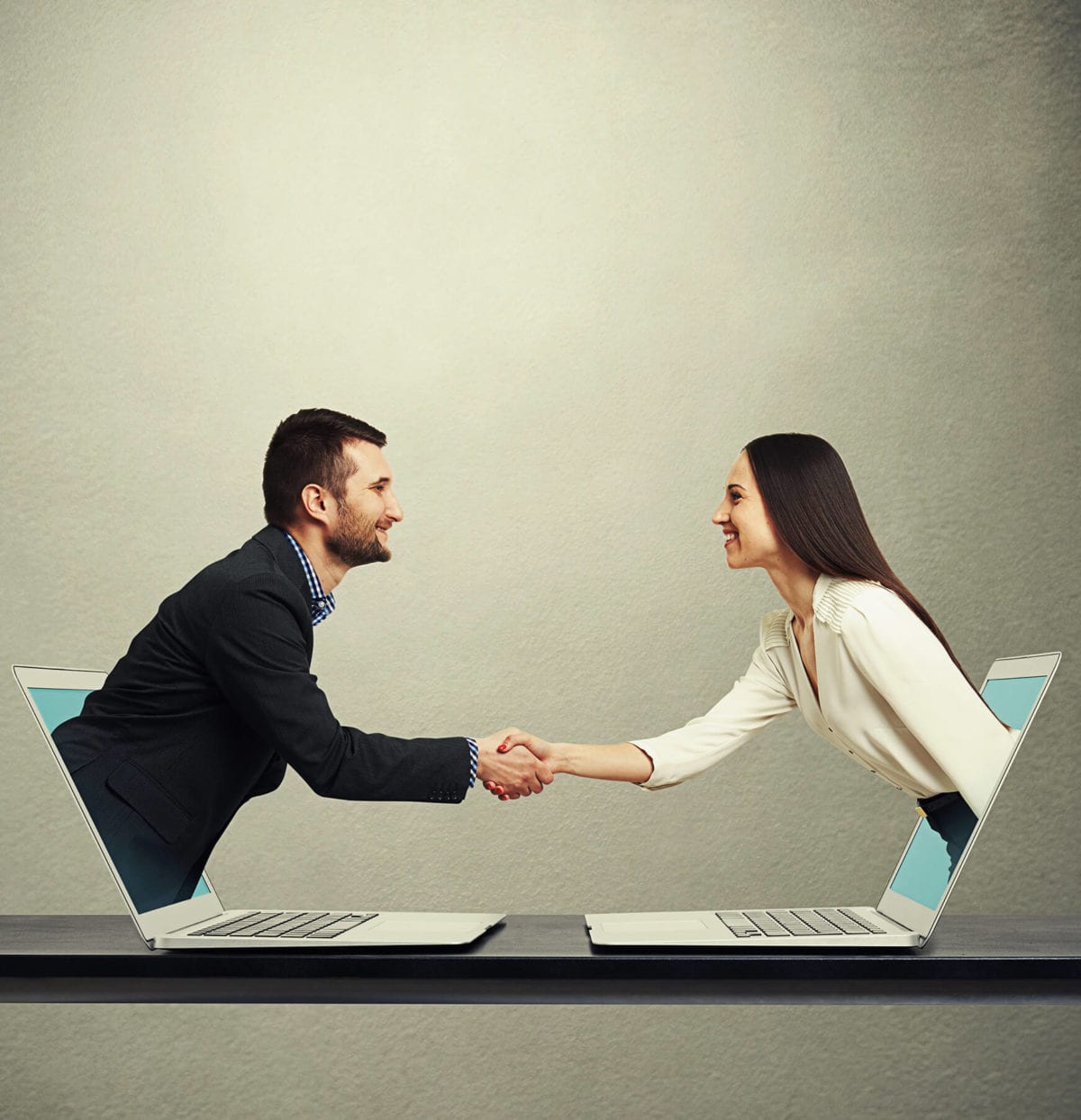 Two professionals shake hands through computers