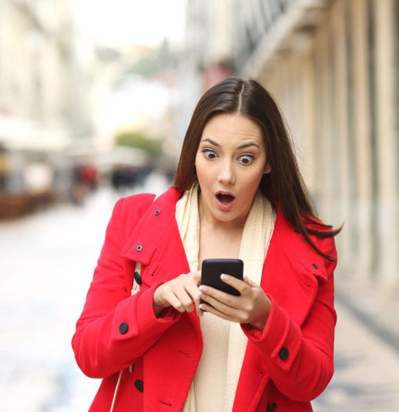 Woman walking in city looks at her phone in surprise
