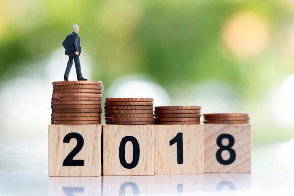 Man figurine standing on pennies on top of blocks reading "2018"