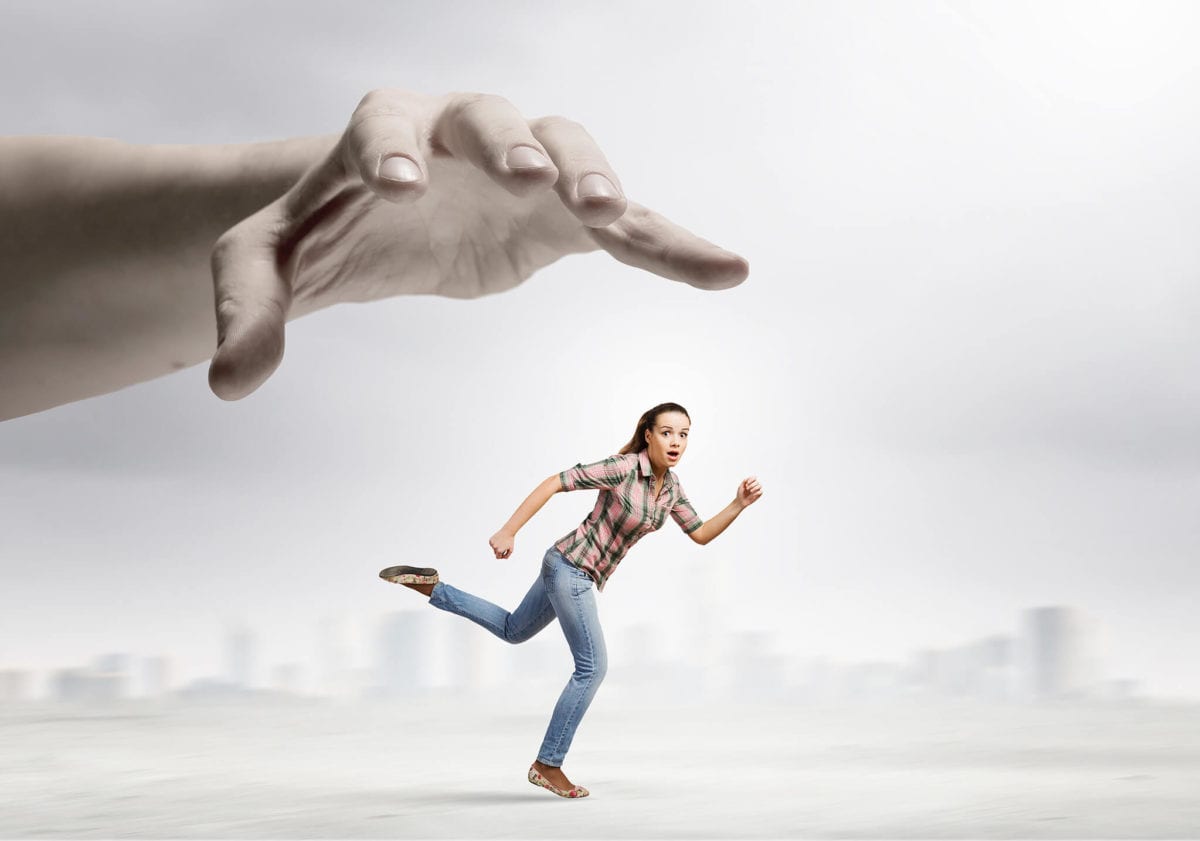 Woman running from large hand