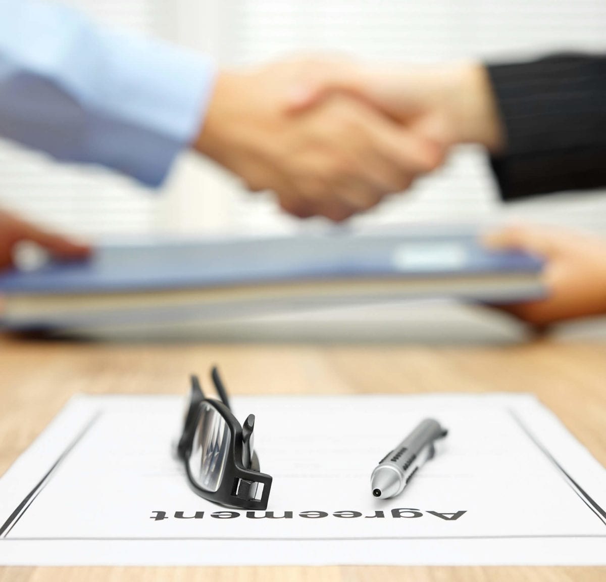 Hands shake behind an agreement on the desk.