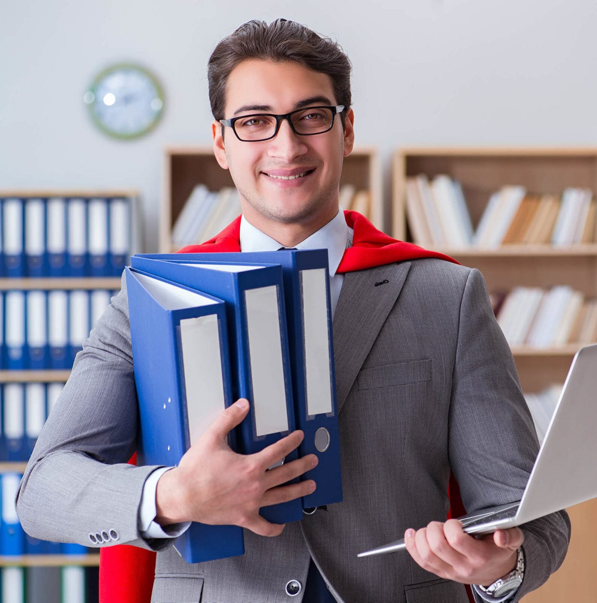 Young businessman wears a cape while holding a computer and files