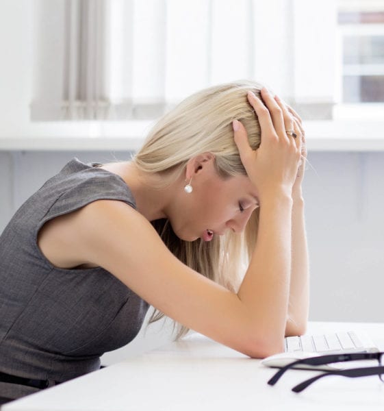 Woman sits at her desk with her hands on her head