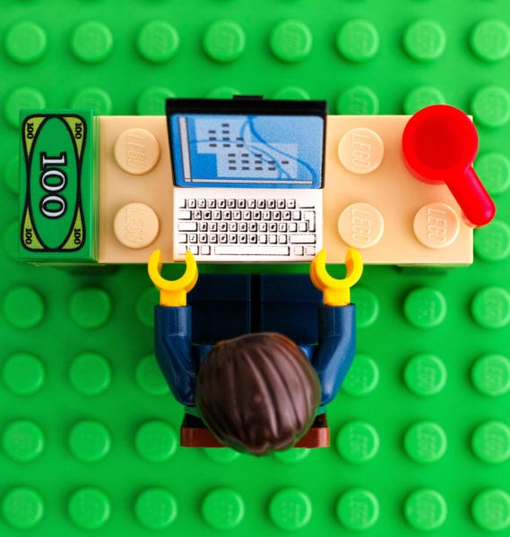 Lego toy business man sits at desk in front of computer