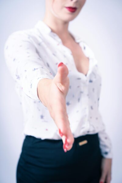 HR recruiter extending hand for handshake, wearing white blouse and black skirt in professional interview setting.