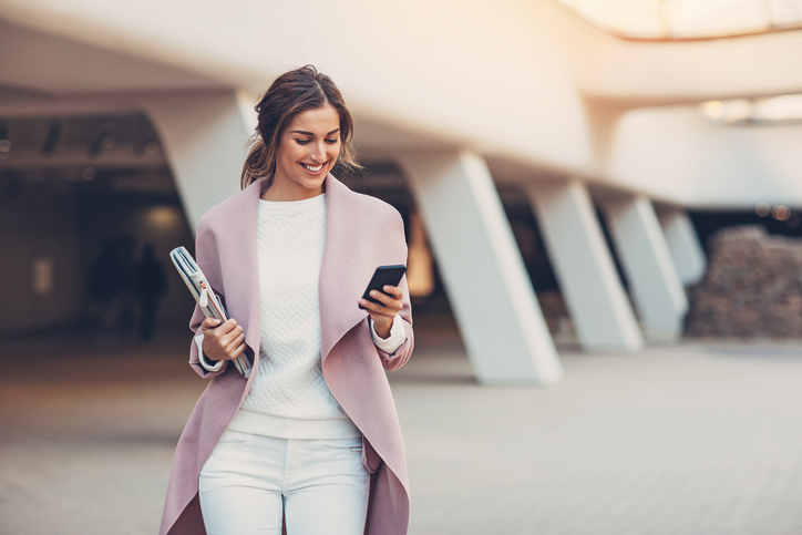 Mobile recruiting candidate reviewing job opportunities on a smartphone while walking outside an office building.